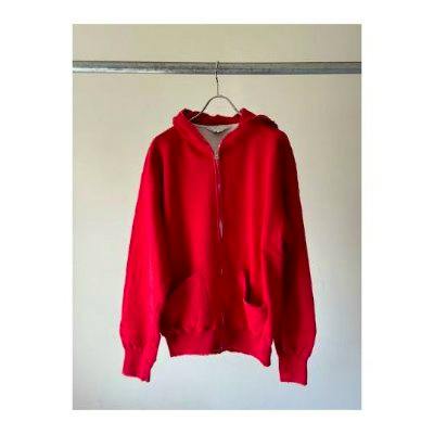 Red zip-up hoodie hanging on a hanger against a plain light-colored wall.