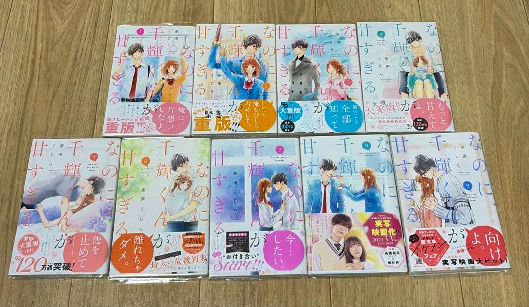 Photograph of volumes 1–9 of the manga "なのに、千輝くんが甘すぎる。」 laid out on a wooden floor.