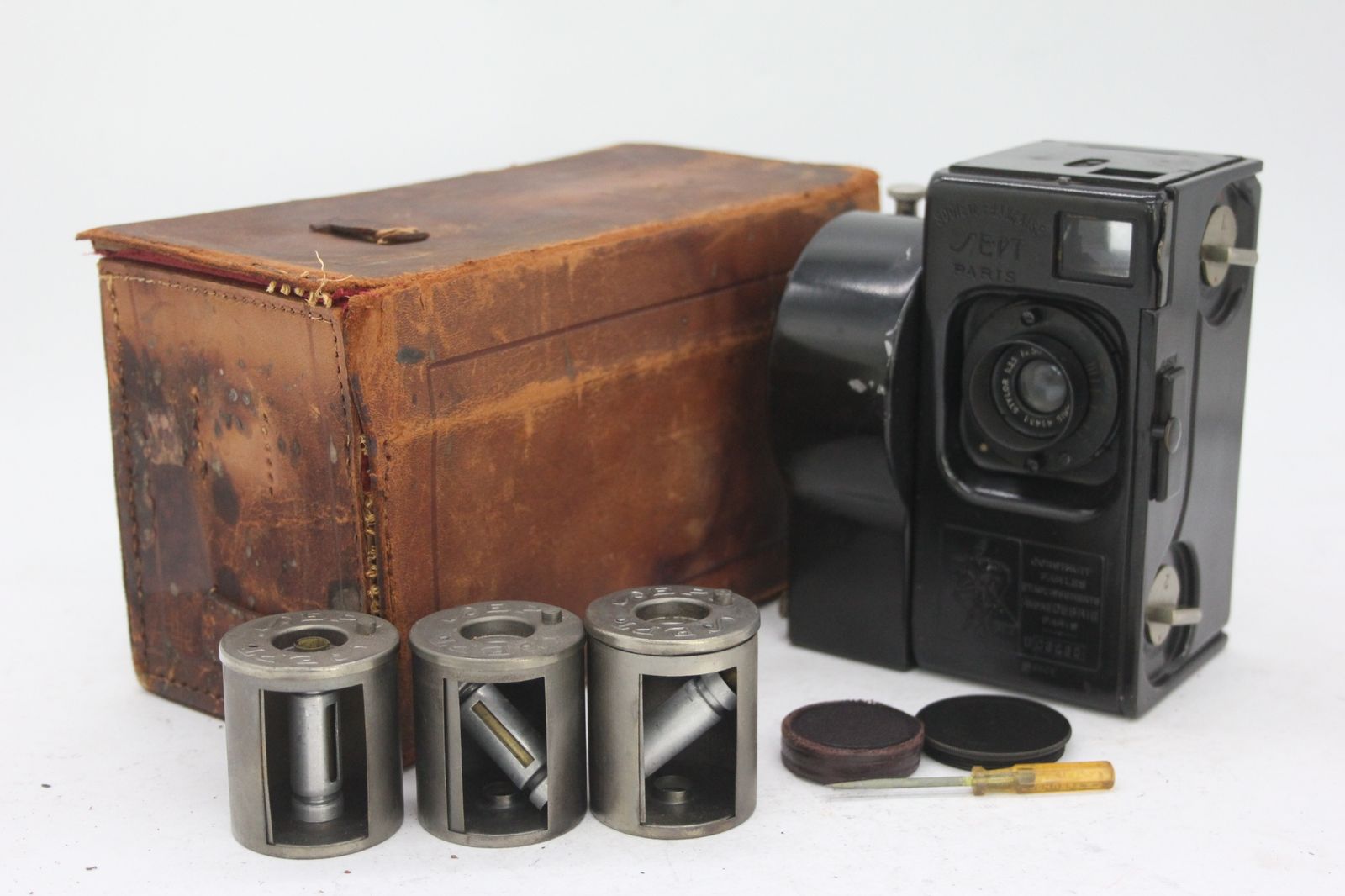 Andre Debrie Societe H.Roussel Stylor 50mm F3.5 35mm film camera displayed with a worn leather case, three metal film cartridges, and small accessories on a white background.