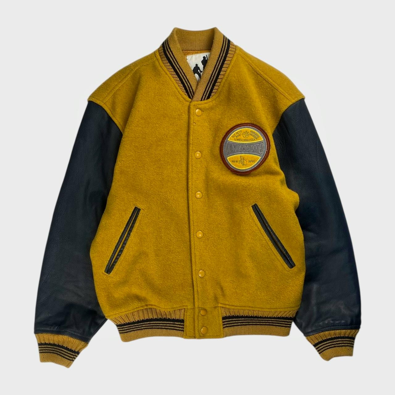 Front view of a men's cow leather stadium jacket with mustard wool body, black leather sleeves, and a round chest patch.