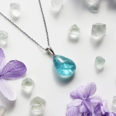 Photo of the necklace showing a blue teardrop pendant on a chain surrounded by crystal-like stones and purple flowers.
