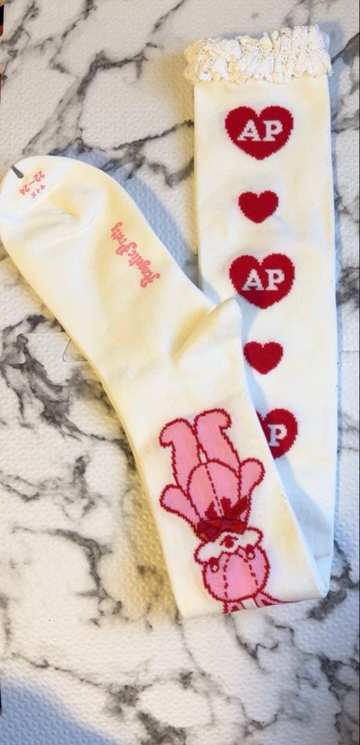 White Angelic Pretty over-the-knee cotton socks laid flat, showing red heart ‘AP’ motifs, a pink bunny design, and lace trim.