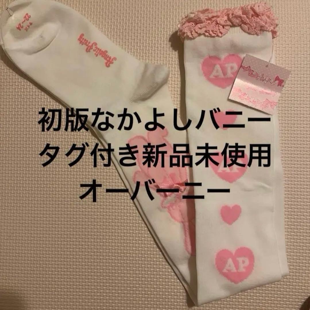 White over-the-knee socks with pink heart "AP" motifs and a hanging tag laid flat.