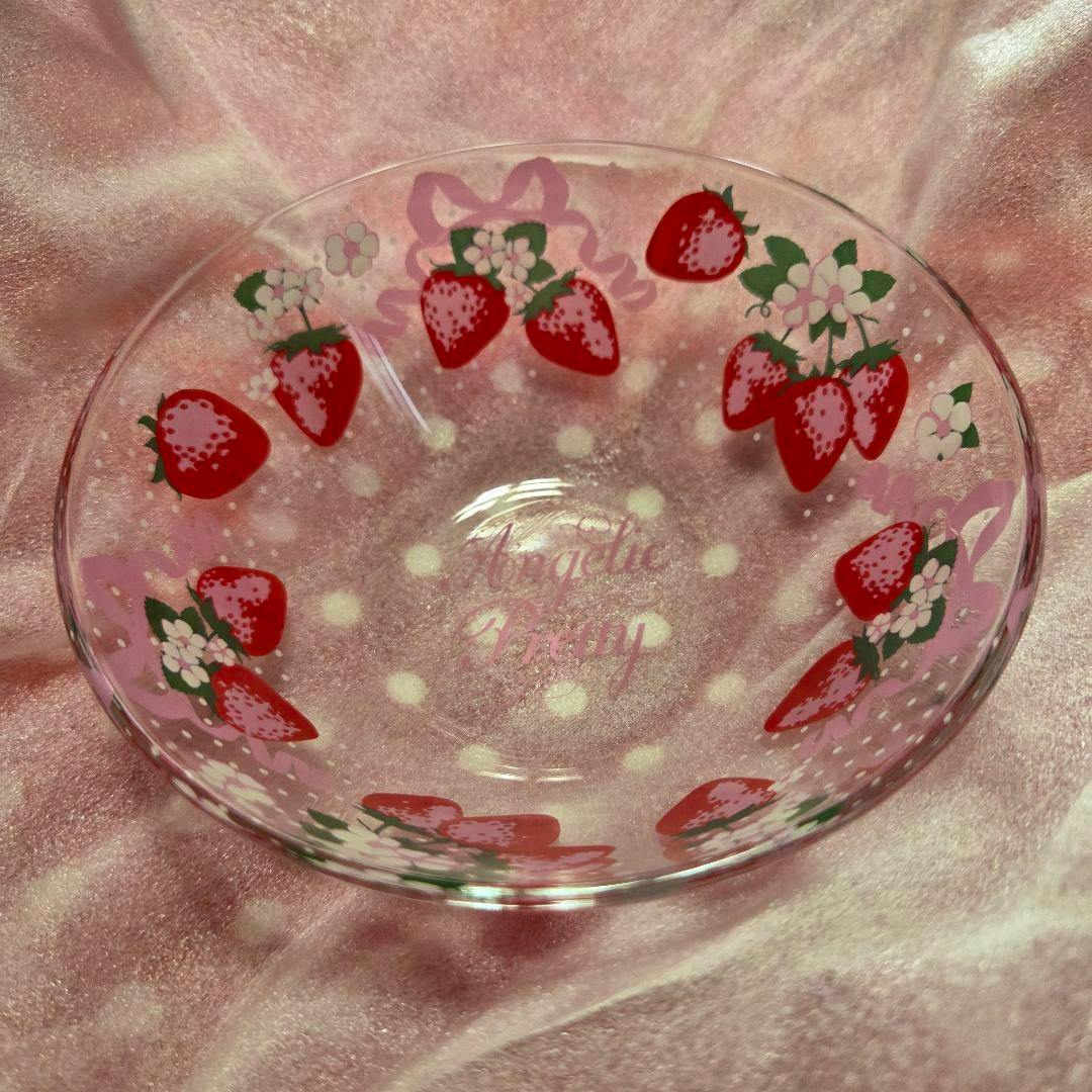 Clear glass bowl decorated with red strawberries, floral accents, and an "Angelic Pretty" script on a pink fabric background.