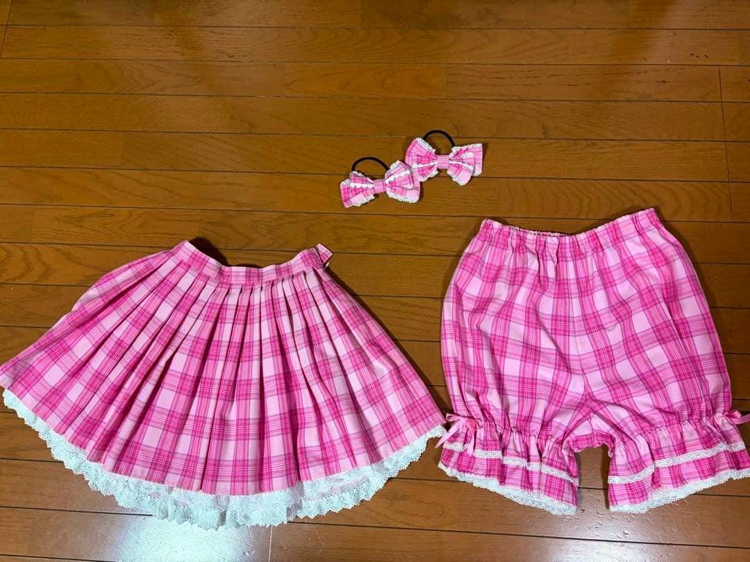 Pink check skirt with matching bloomers/drawers and ribbon hair ties laid flat on a wooden floor.