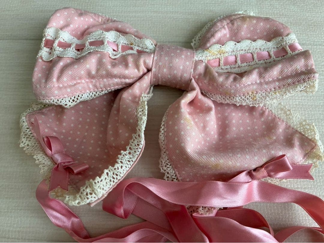 Pink polka-dot ribbon headdress with lace trim and long satin ties displayed flat.