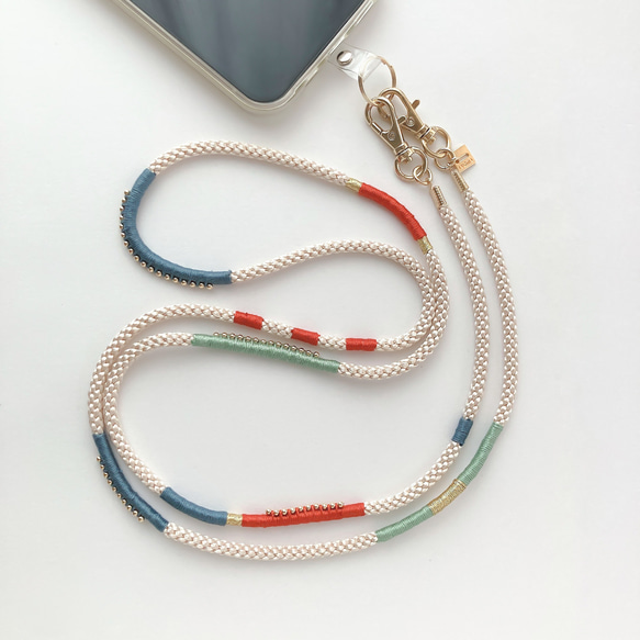 A cream braided polyester phone shoulder strap with blue, red, and green stitched accents attached to a smartphone.