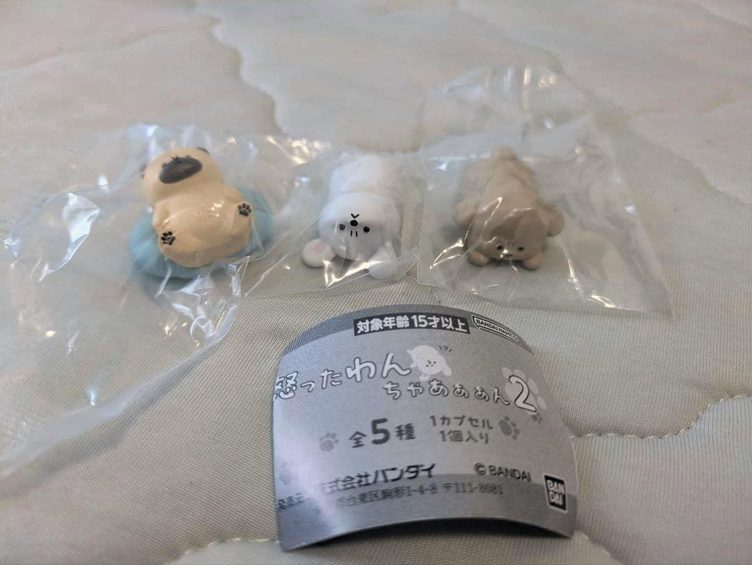 Photo of three small dog figure toys individually sealed in clear plastic bags with a folded paper insert on a light surface.