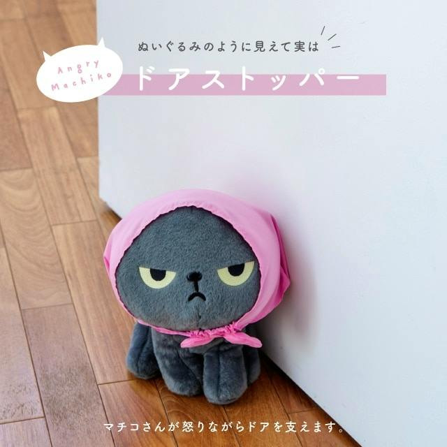 Angry Machiko gray plush door stopper wearing a pink headscarf placed against a door on a wooden floor.