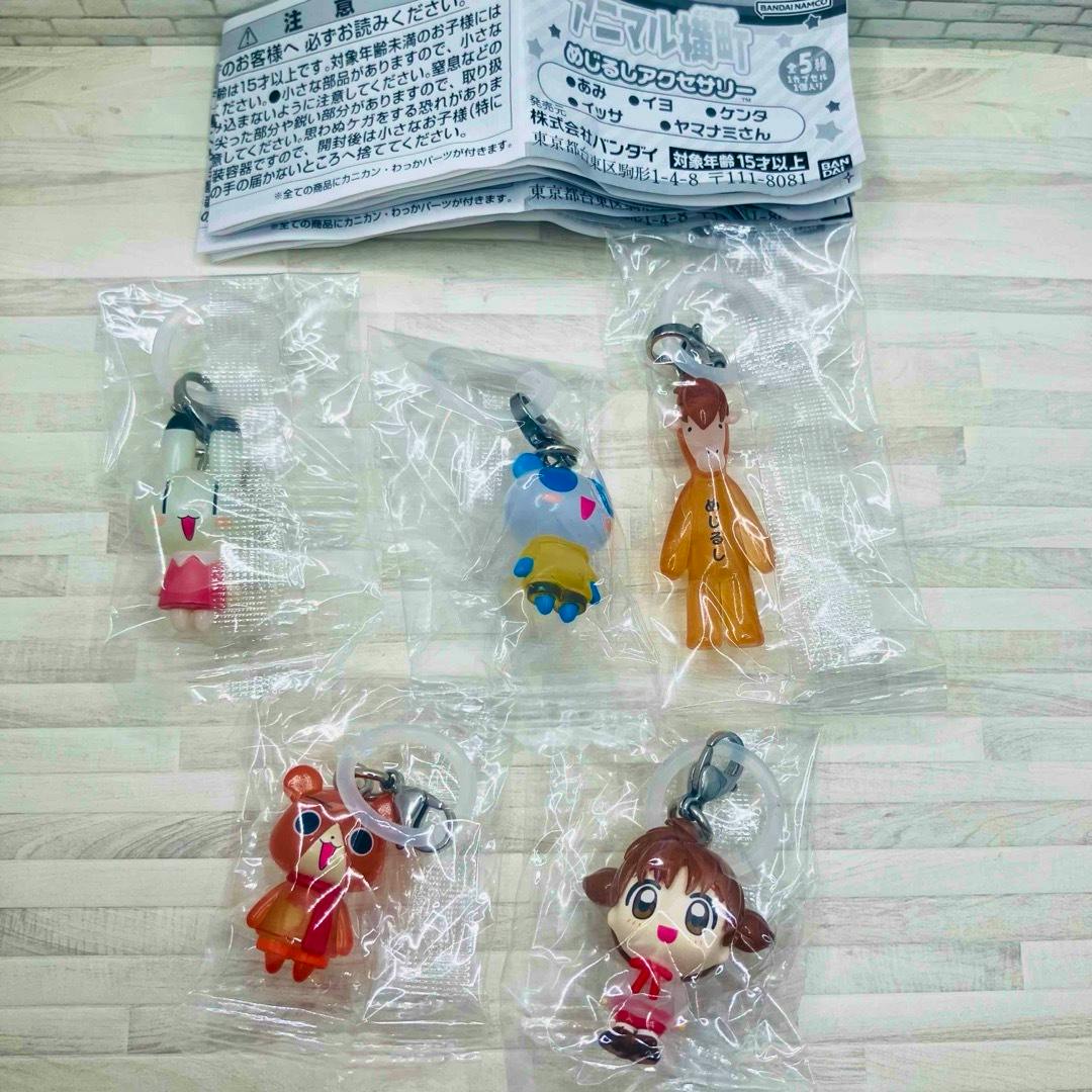 Five individual plastic keychain mascots from the Animal Yokochō complete set, each sealed in a clear bag and arranged on a light wooden surface with the folded instruction sheet visible.
