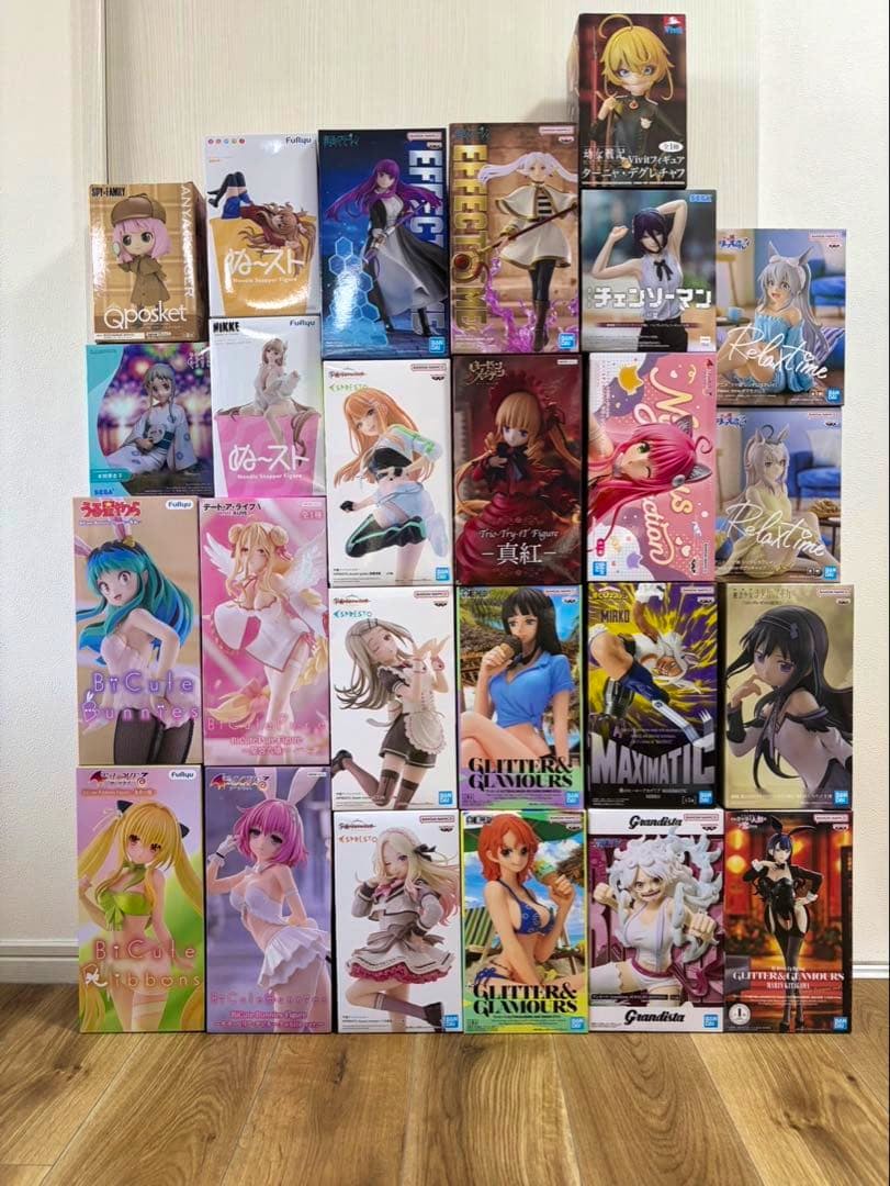 Photograph of 25 boxed anime girl figures arranged in a stacked grid against a wall on a wooden floor.