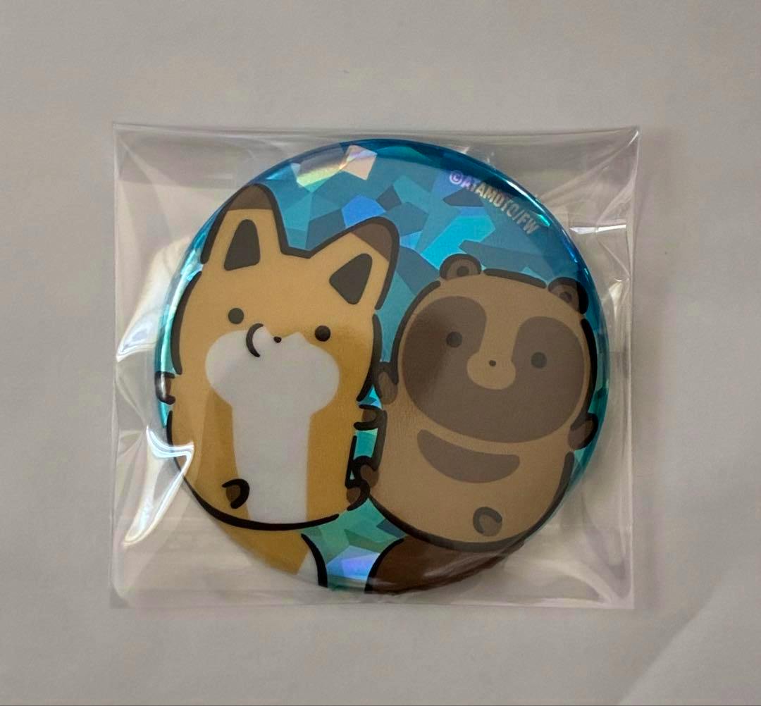 Round holographic can badge depicting Tanuki and Kitsune characters in sealed clear plastic packaging.