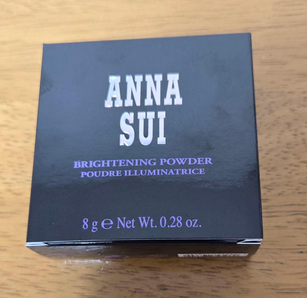 Front view of a boxed ANNA SUI Brightening Powder showing the brand name and net weight.