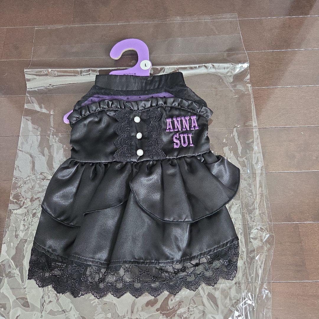Front view of a black satin ANNA SUI dog dress with lace trim on a purple hanger labeled L.