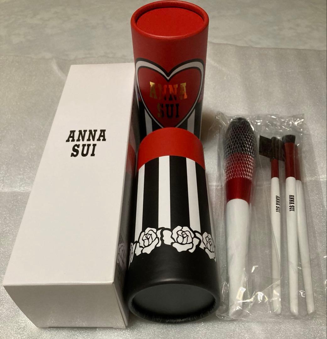 Anna Sui makeup brush set showing a striped cylindrical brush case, a white Anna Sui box, and four brushes in a plastic sleeve.