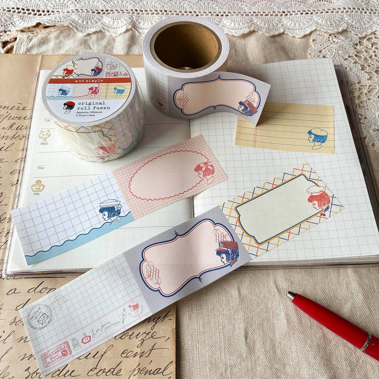 Roll of decorative roll sticky notes (ant simple) with several labels unrolled and placed on an open notebook.