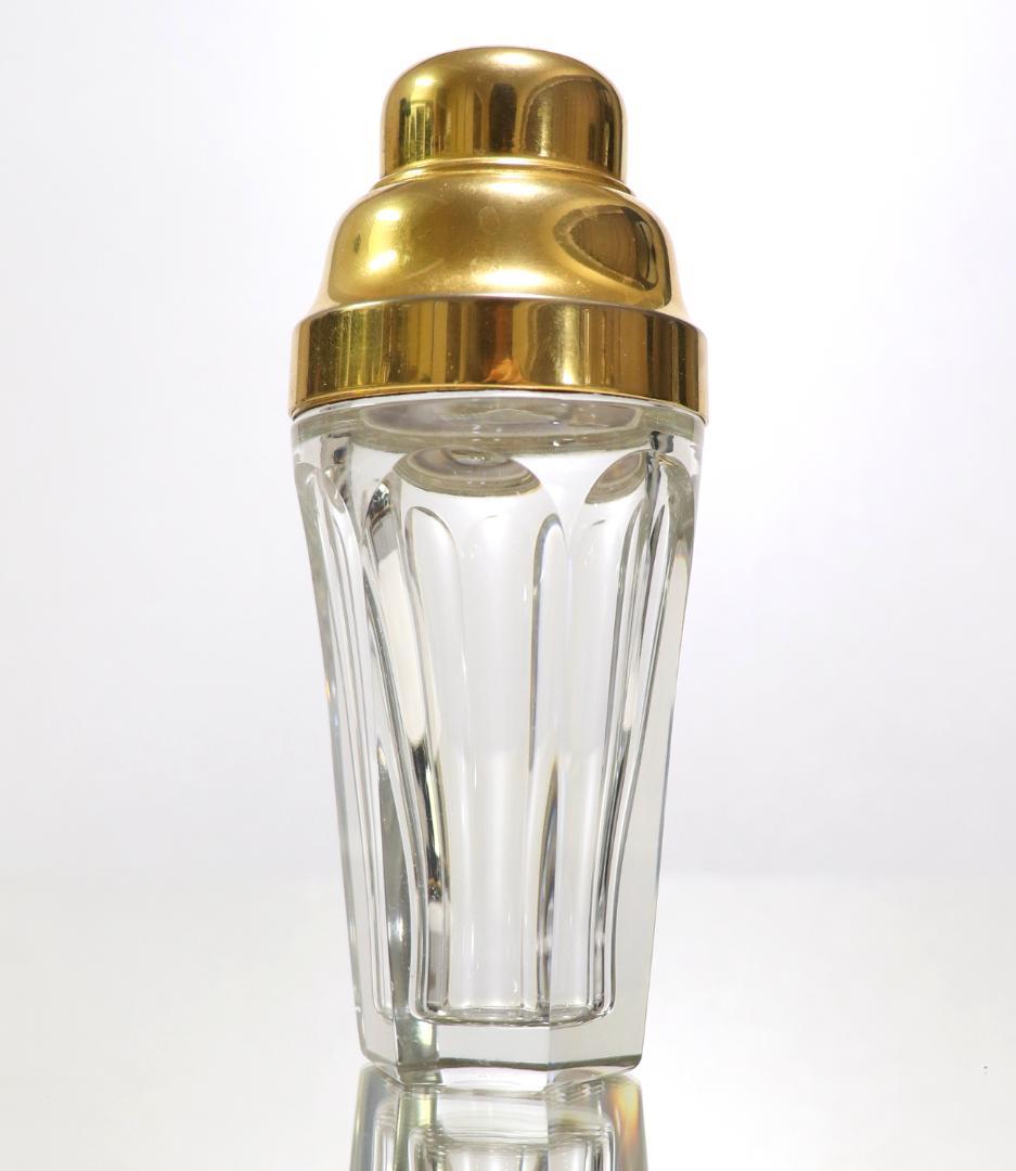 Clear Old Baccarat crystal perfume bottle with gold-colored cap and decoration on a white background.