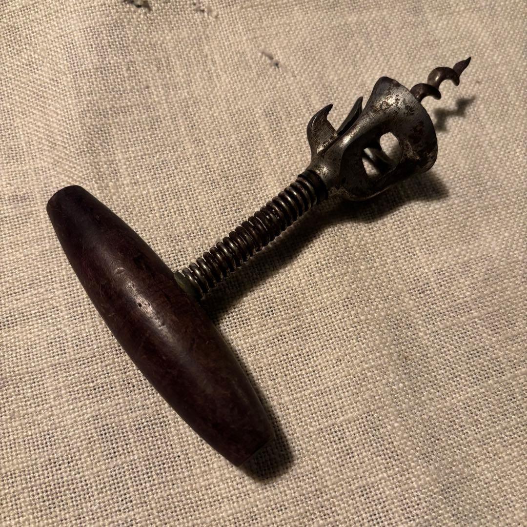 Antique corkscrew with a wooden T-handle and metal screw and opener shown on fabric.