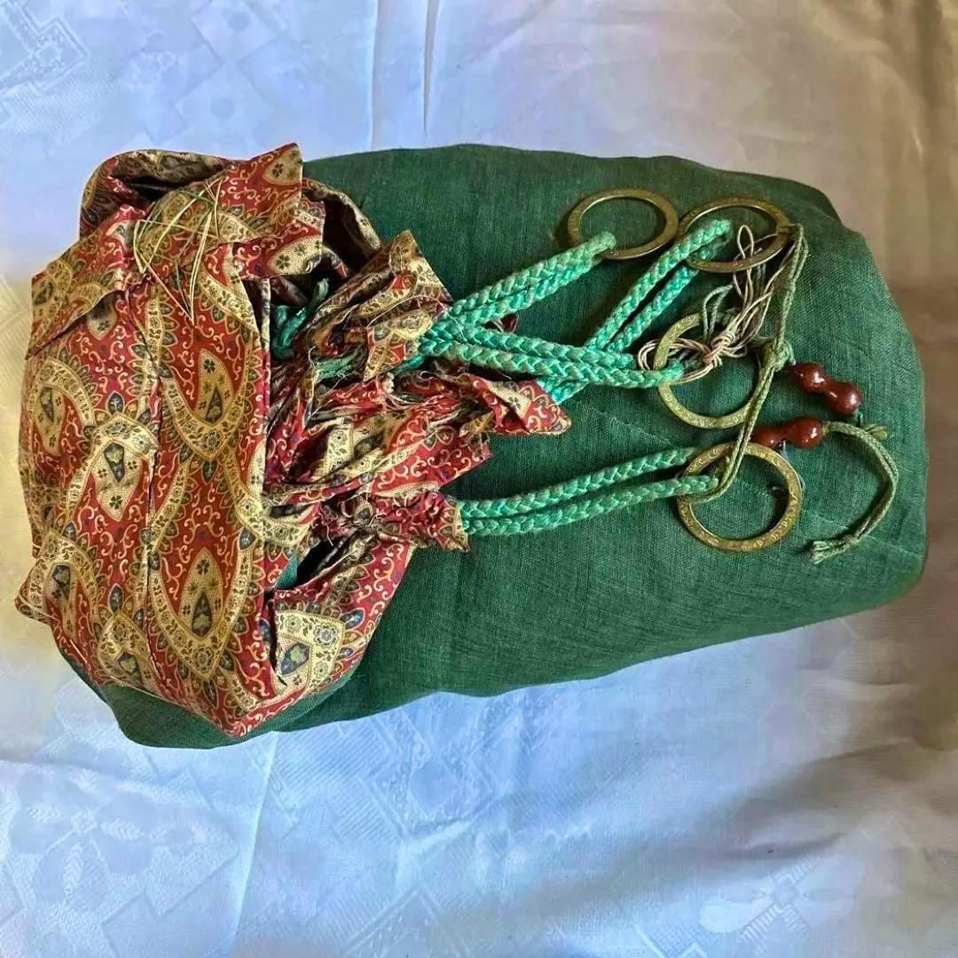 Folded antique extra-large mosquito net in green with patterned red trim, braided green cords, and metal rings.