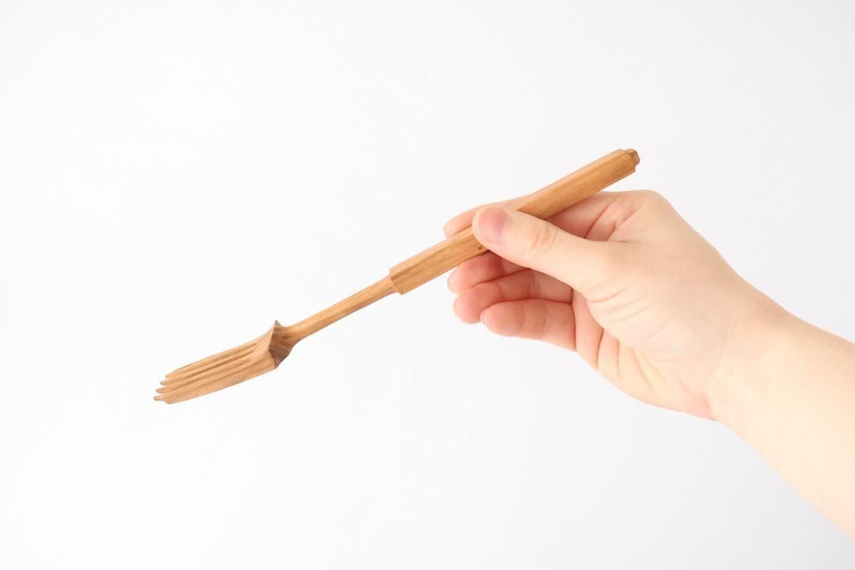 A wooden fork held in a hand against a plain white background.