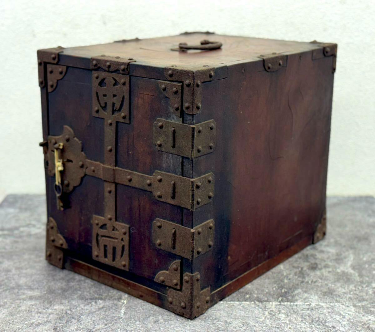 Wooden drawer chest with metal corner hardware and a front lock, shown closed on a gray surface.