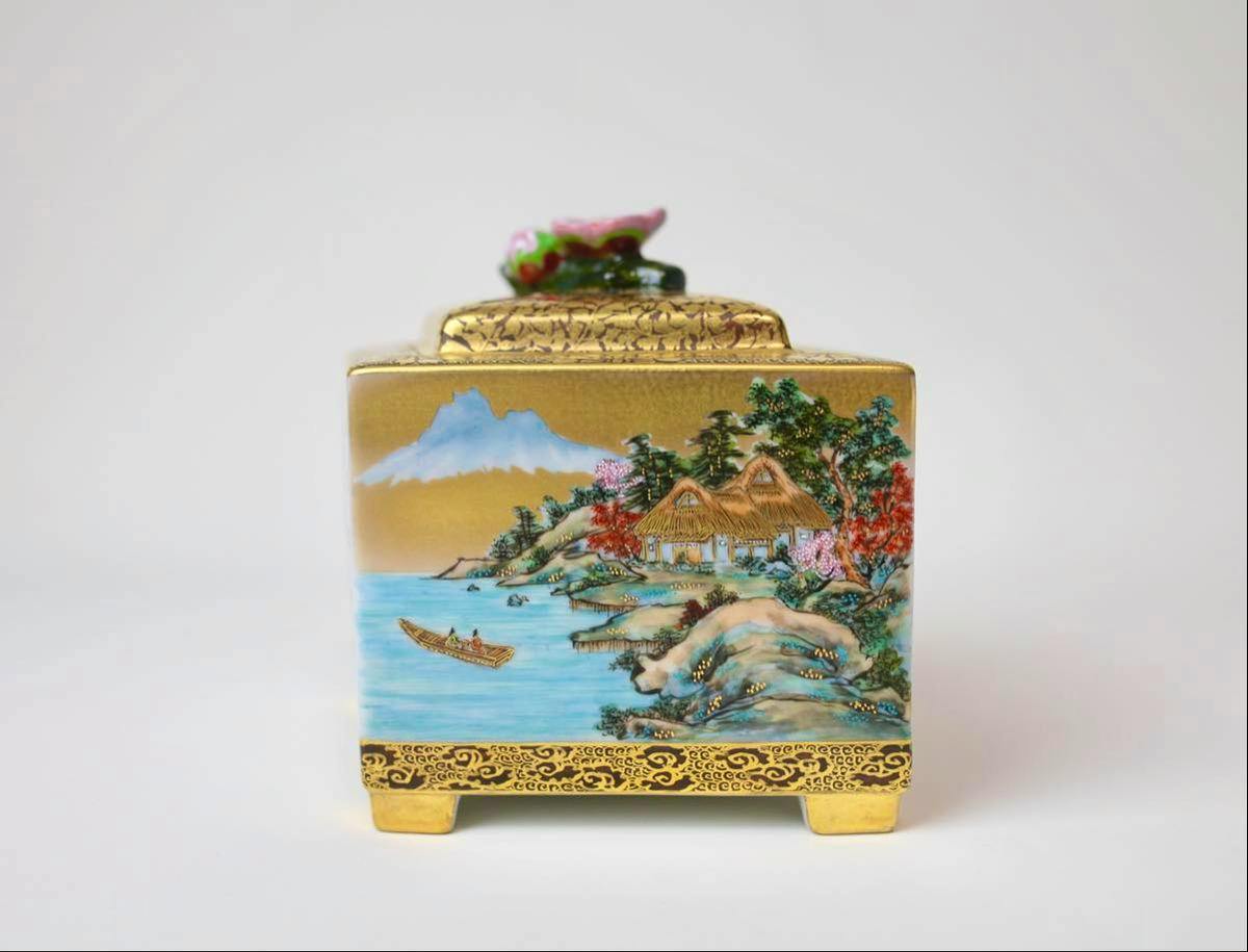 Front view of a square Kutani-yaki ceramic incense burner with gold trim and a painted coastal landscape scene.