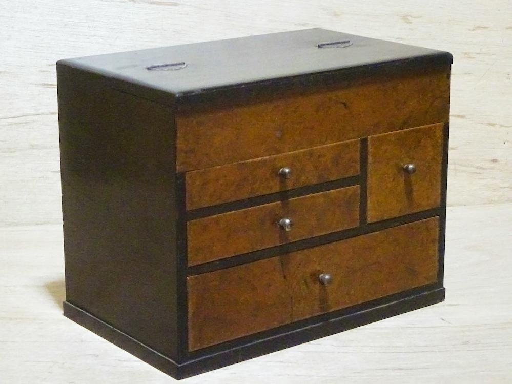 Front three-quarter view of a small wooden sewing box (storage chest) with multiple drawers and round knobs.