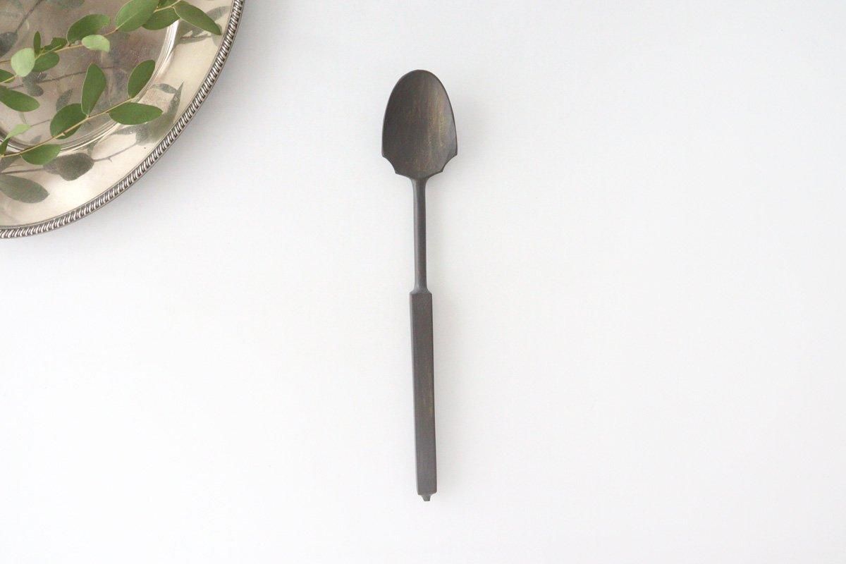 Antique metal spoon with a long rectangular handle shown on a white background.
