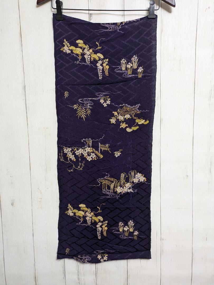 A long purple silk kimono fabric panel with gold and white floral patterns hanging from a hanger against a white wooden background.