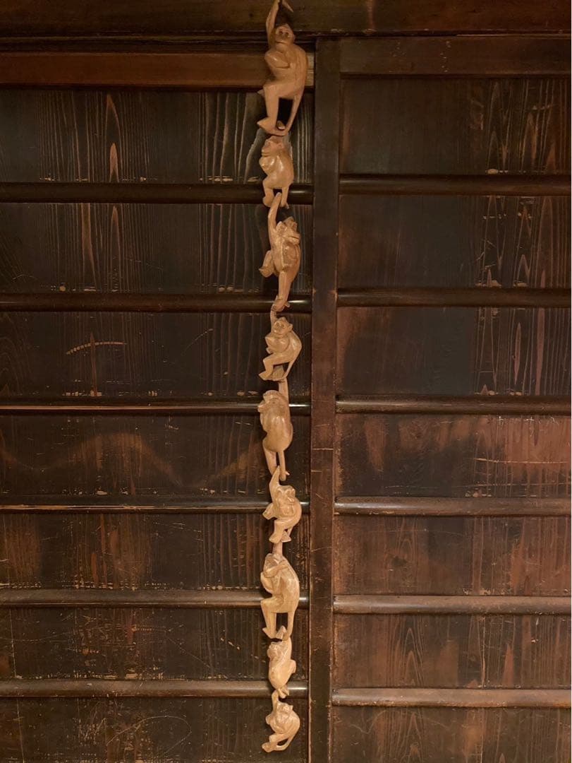 A full-length wooden hanging ornament showing multiple carved monkeys strung vertically against a wooden background.
