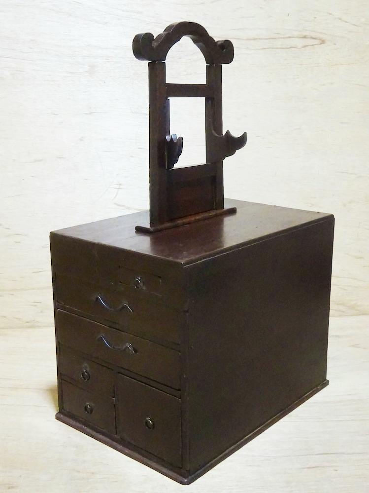 Front three-quarter view of the small wooden storage chest showing multiple drawers and a mirror stand mounted on top.