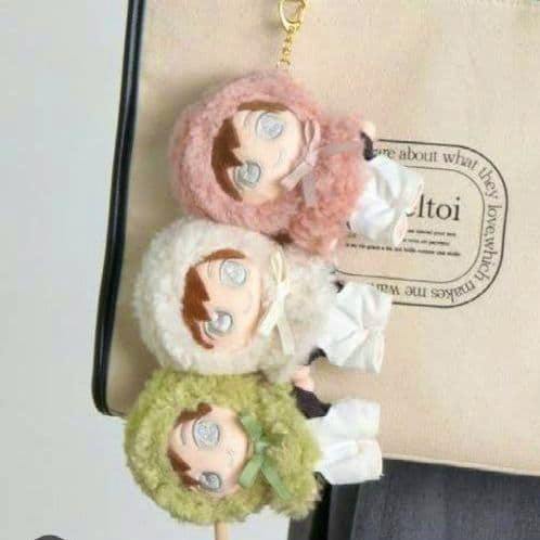 Three small plush dolls wearing fluffy hooded doll clothes in green, white, and pink.