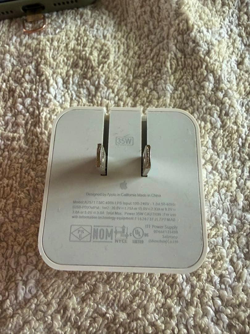 White Apple 35W power adapter showing its folded US prongs and regulatory text on the back.