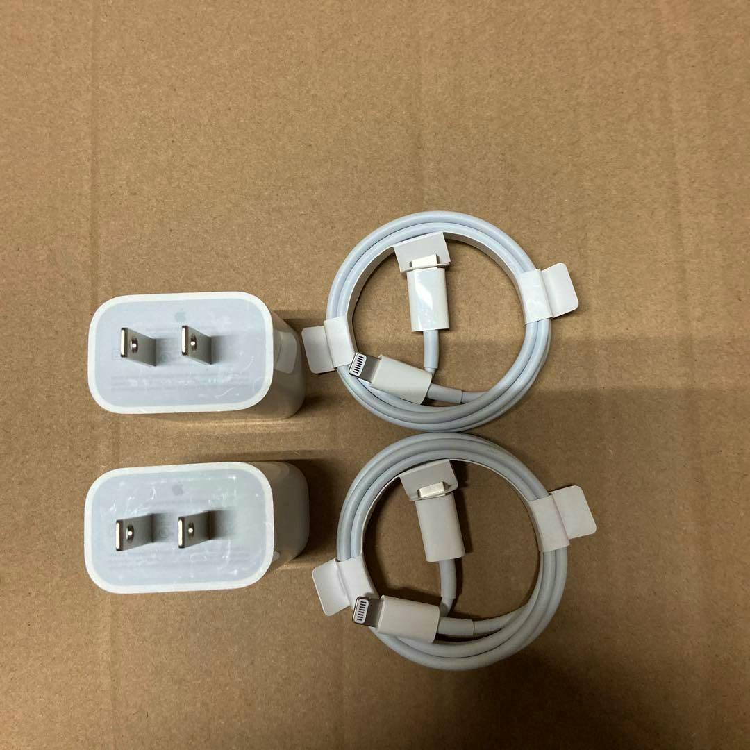 Two Apple 20W chargers and two coiled USB-C to Lightning cables arranged on a cardboard surface.