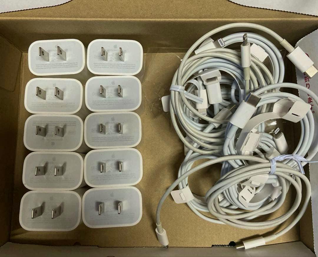 Ten white Apple 20W USB-C power adapters and multiple white charging cables coiled inside a cardboard box.