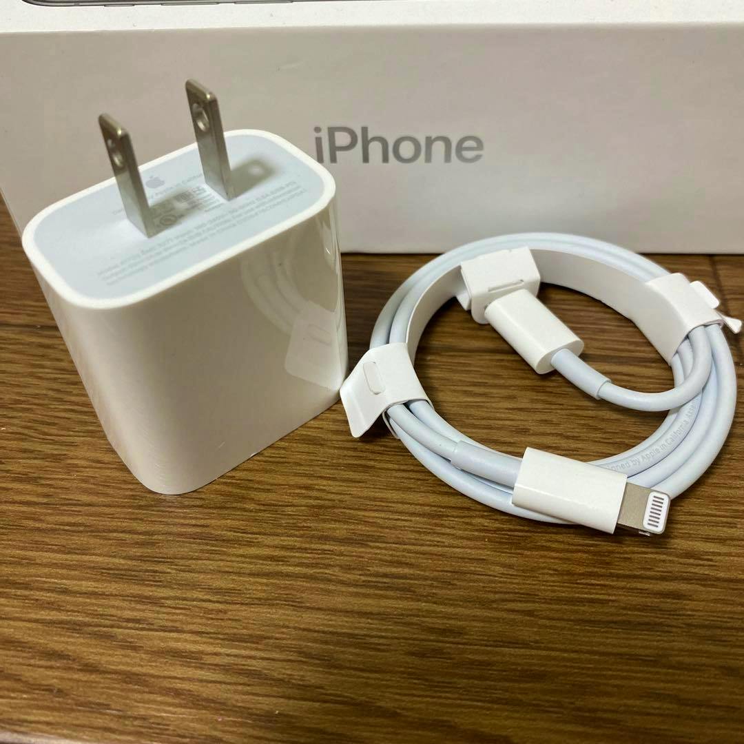 Apple white USB-C power adapter and coiled Lightning cable on a wooden surface with an iPhone box behind them.
