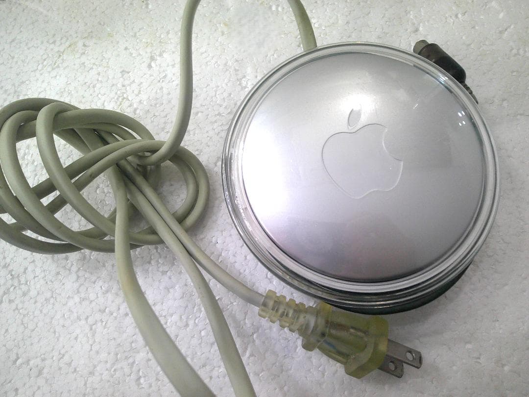 Round silver Apple portable power adapter (M7332) with attached gray cable and two-prong plug on a white background.