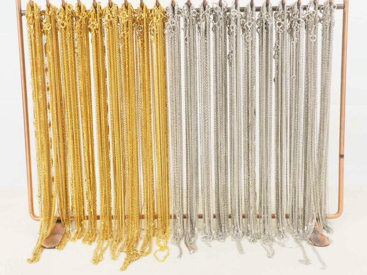 Many gold and silver necklace chains hanging from a display rack.
