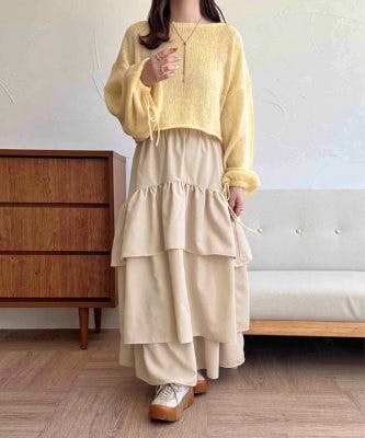 Model standing wearing a beige tiered women's skirt styled with a yellow sweater and platform sneakers.