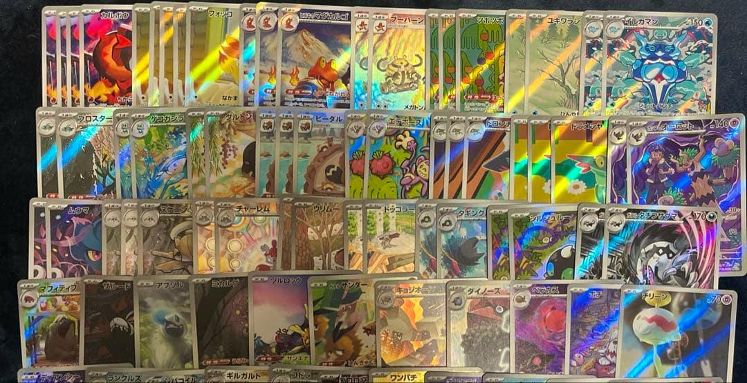 A large assortment of holographic trading cards arranged in rows on a dark background, showing various card artworks.