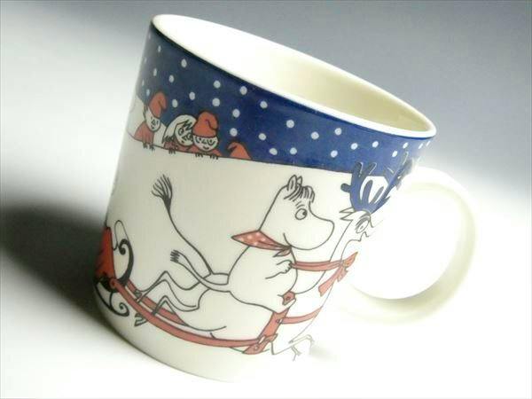 Ceramic mug showing Moomin characters riding a sleigh with a blue polka-dot rim.