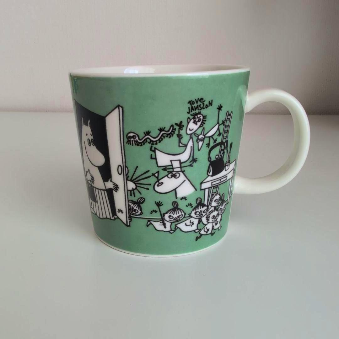 Green Moomin drawing mug showing black-and-white illustration wrap and a white handle.