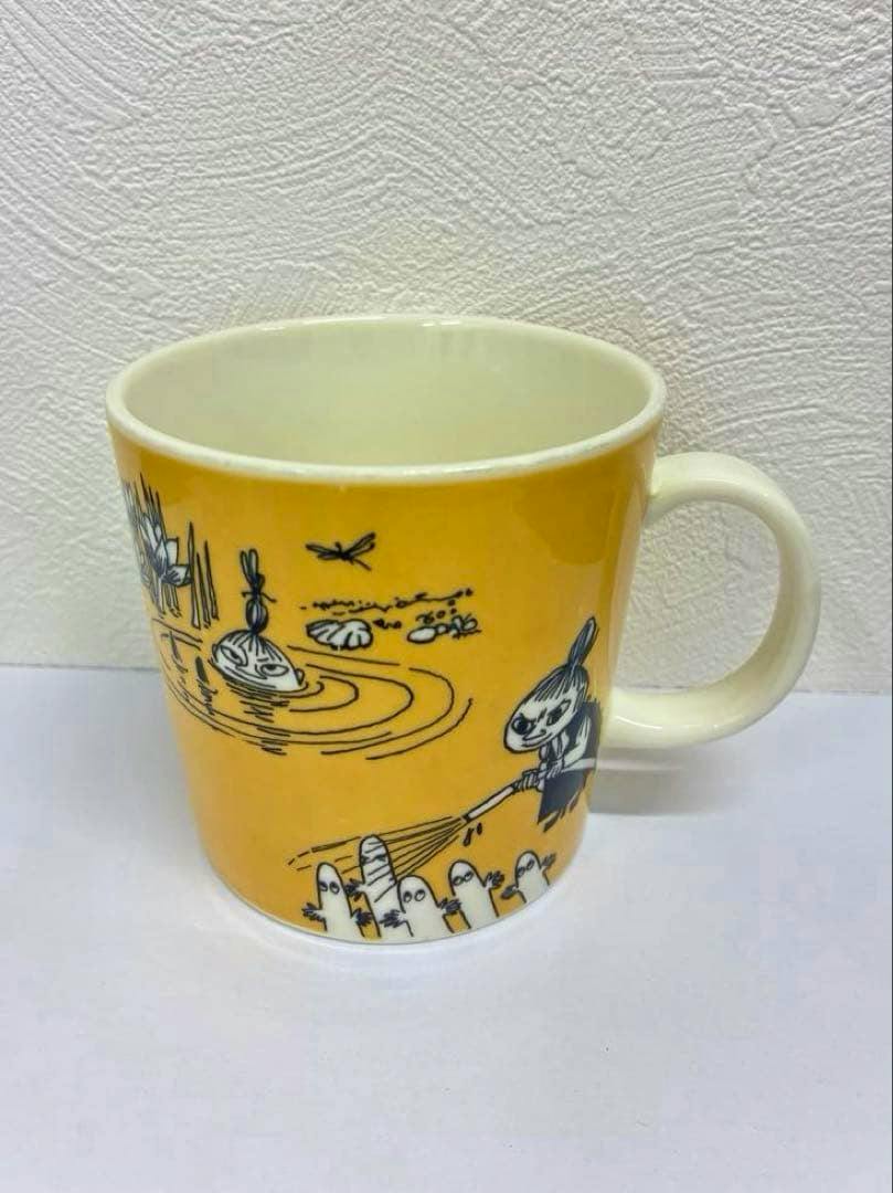Yellow ARABIA Moomin ceramic mug with printed Moomin characters, shown from a front-right angle.