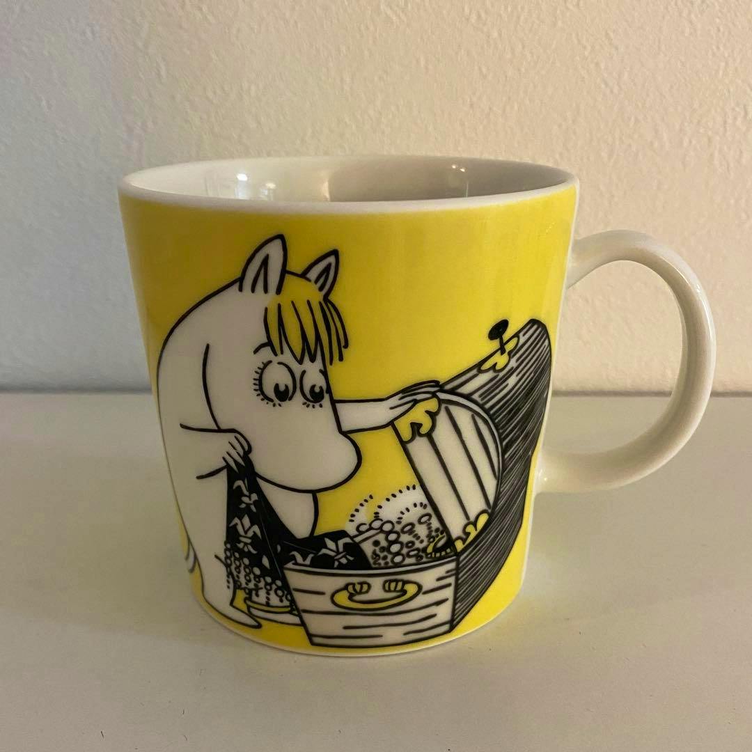 Yellow Arabia Moomin mug featuring the character Floreen (Snork Maiden) opening a chest, shown with a white handle.