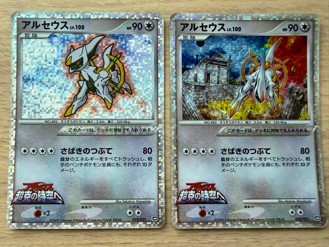 Two Arceus movie promotional trading cards shown side-by-side on a wooden surface.