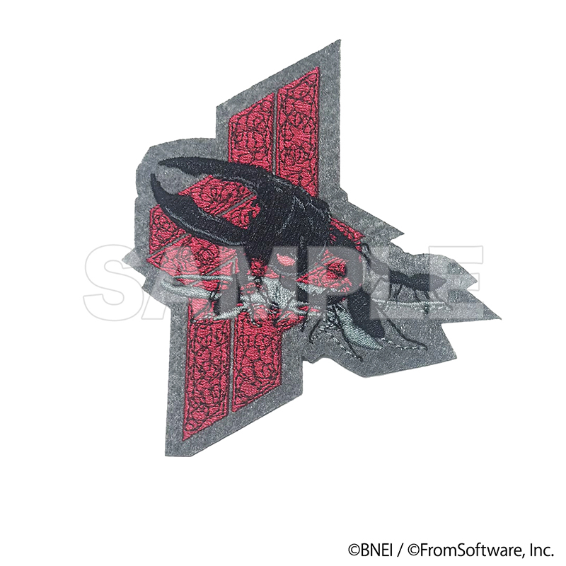Photograph of the ARMORED CORE VI original fabric patch (G5イグアス) showing an embroidered black emblem over a red patterned geometric background.