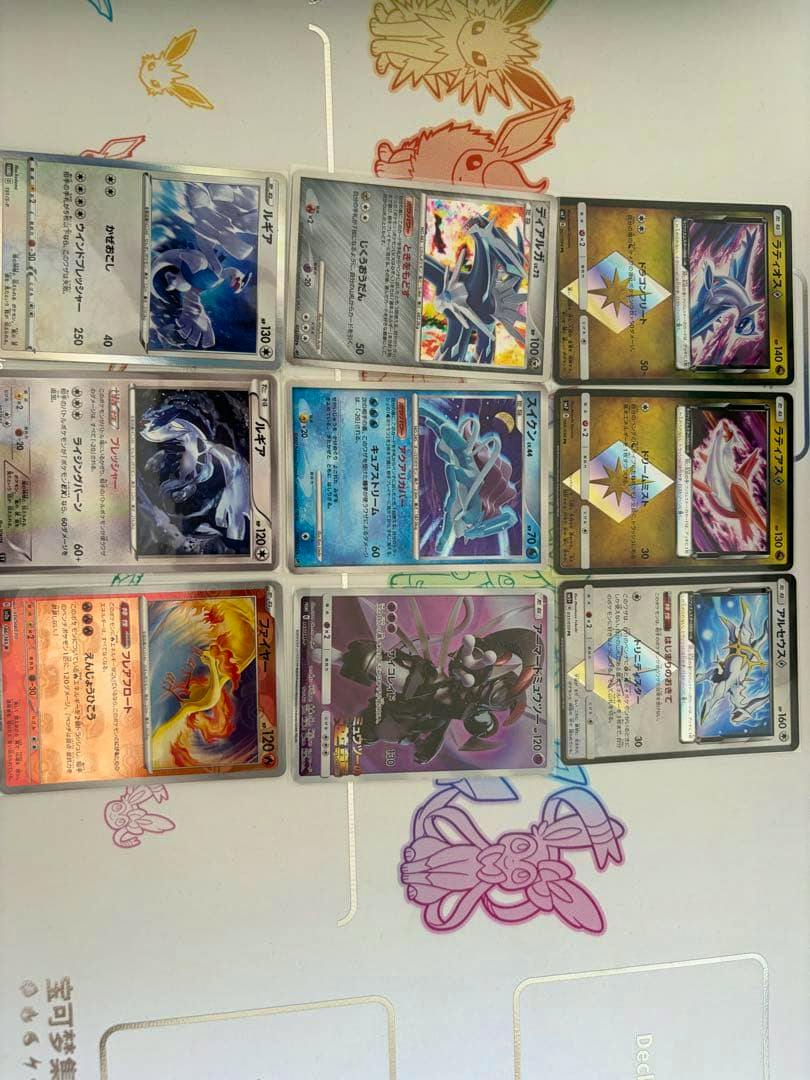 Several Pokémon trading cards, including Lugia, Suicune, and Armored Mewtwo promos, laid out on a playmat.