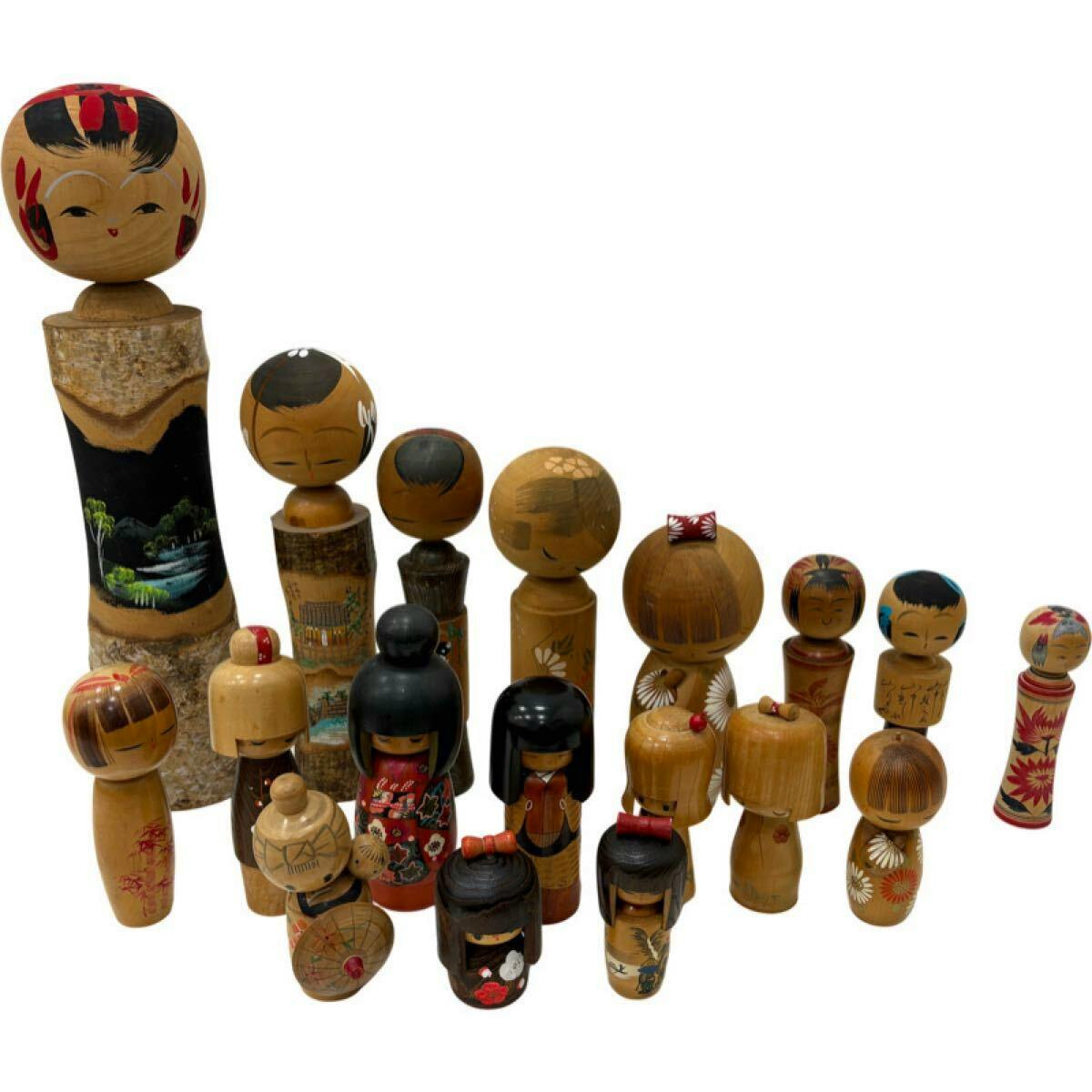 Eighteen traditional wooden kokeshi dolls of varying sizes and painted faces arranged on a white background.
