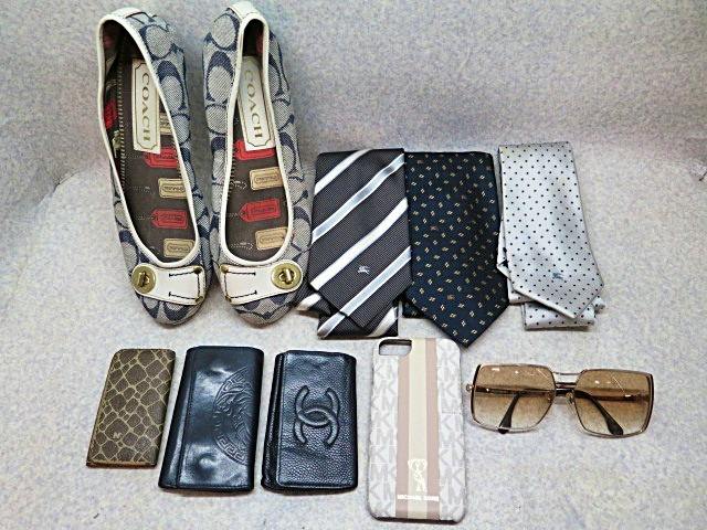 A laid-out assortment of branded accessories including a pair of Coach flats, three ties, several wallets, a phone case, and sunglasses.