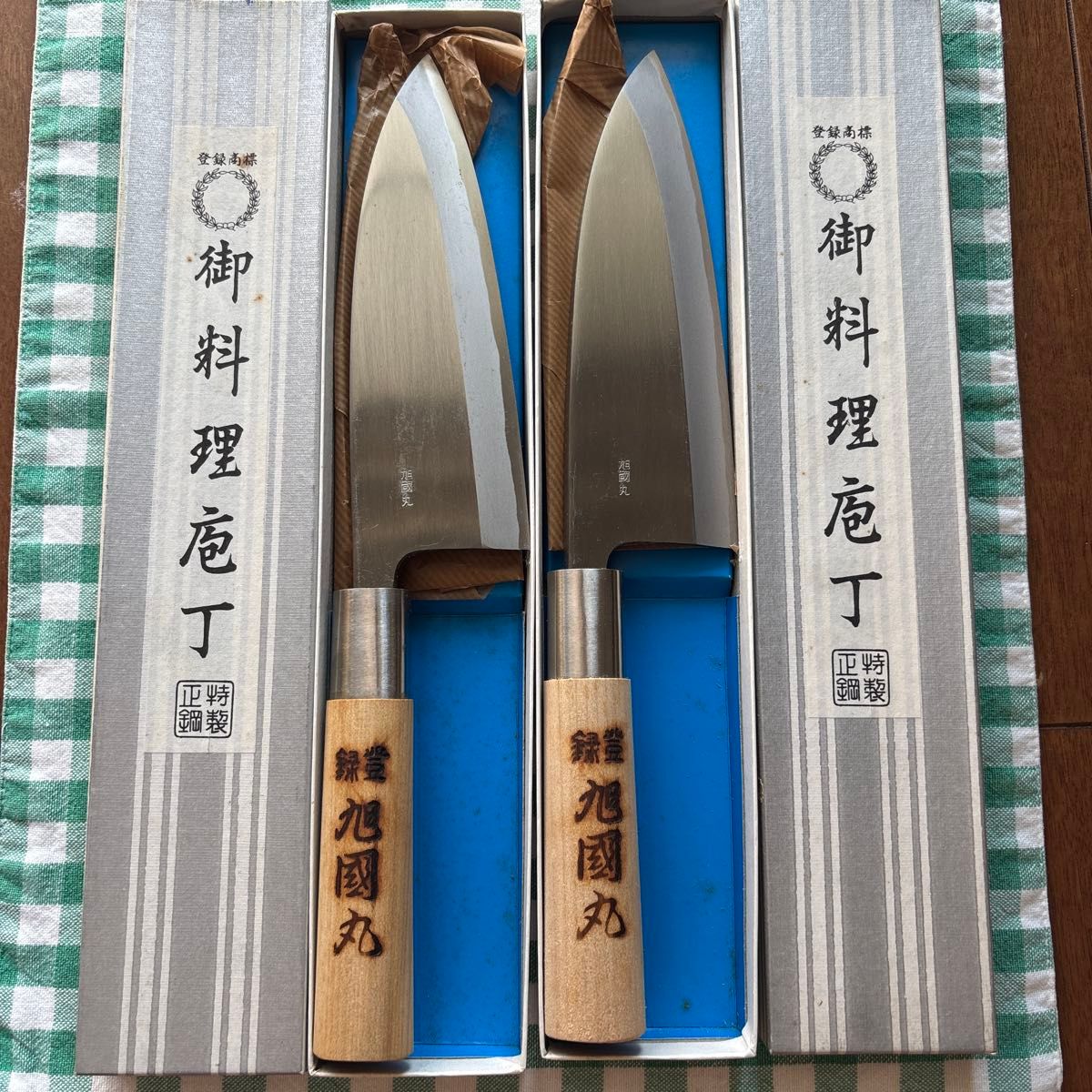 Two Japanese-style chef knives with wooden handles displayed in box compartments, showing the metal blades and Japanese text on the packaging.